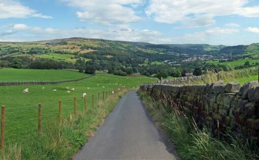 A countryside panorama with a lane running down the middle and a stonewall on one side and a fence on the other