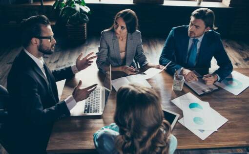 Four business people sitting around a wooden table having a meeting with laptops and charts